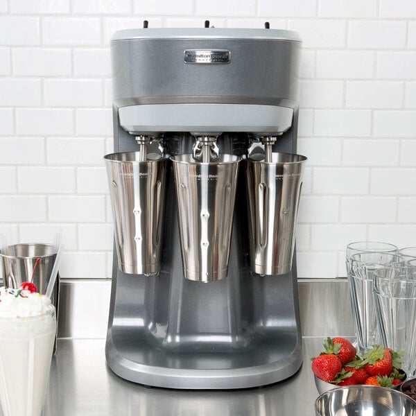 A Hamilton Beach triple spindle drink mixer with silver cups and a cherry on top.