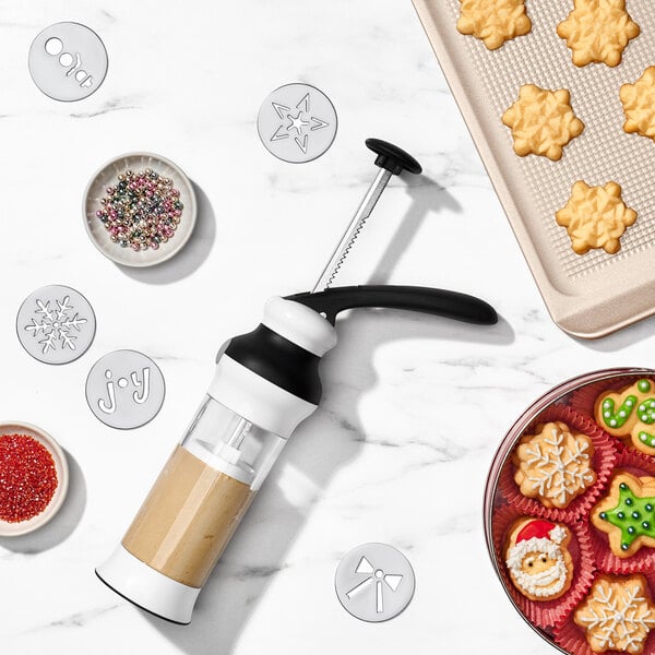 A cookie press and a cookie cutter on a table with cookies.