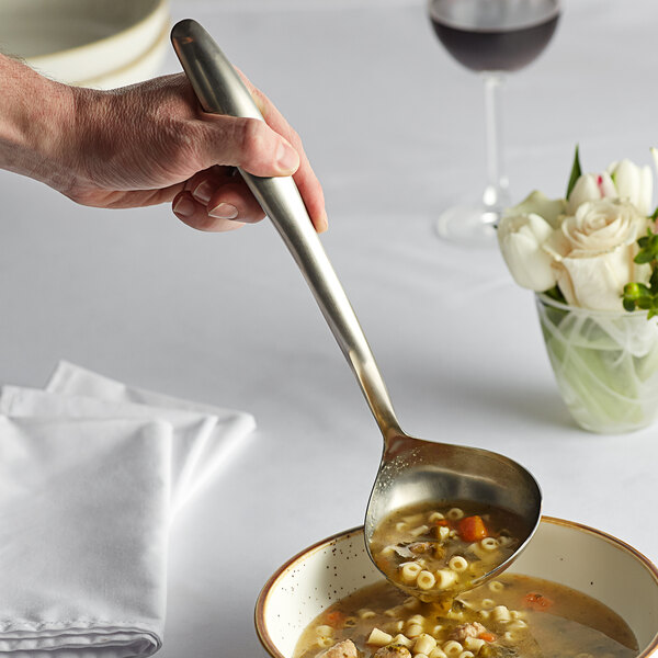 A hand holding a Tablecraft stainless steel soup ladle over a bowl of soup.