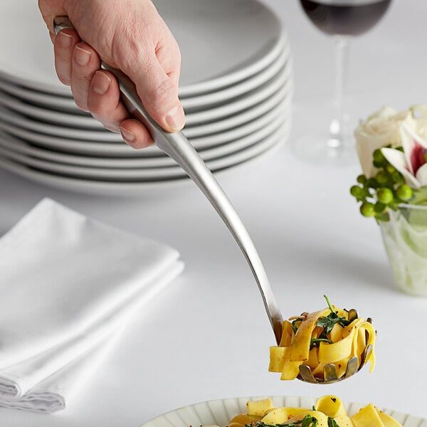 A hand holding a Tablecraft stainless steel pasta grabber over a plate of pasta.
