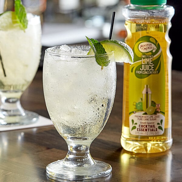 A bottle of Master of Mixes Sweetened Lime Juice on a table with a glass of ice and lime garnish.