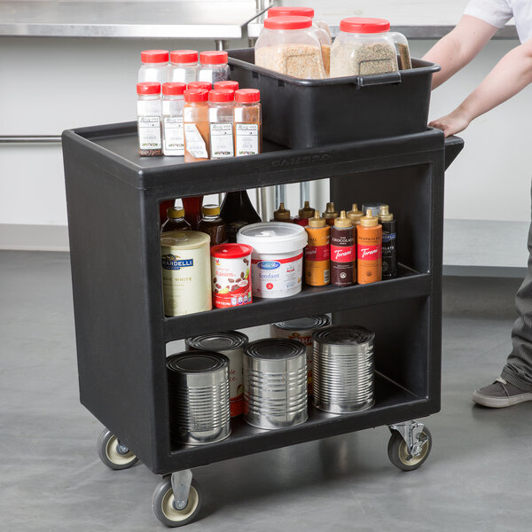 A man using a Cambro black three shelf service cart to hold food and spices.