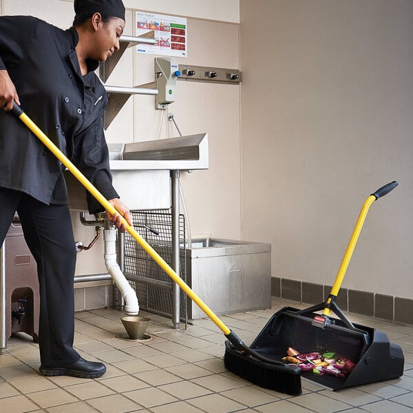 A woman using a Rubbermaid upright dust pan to sweep a floor.