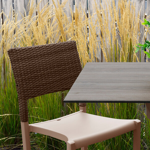 A Grosfillex Java taupe resin sidechair with a wicker back on a table in a garden.