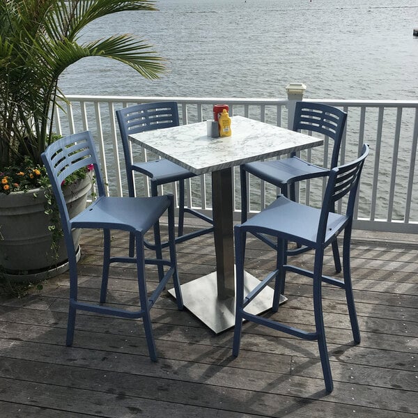 A Grosfillex white marble table top on a wood deck with chairs and a potted plant.