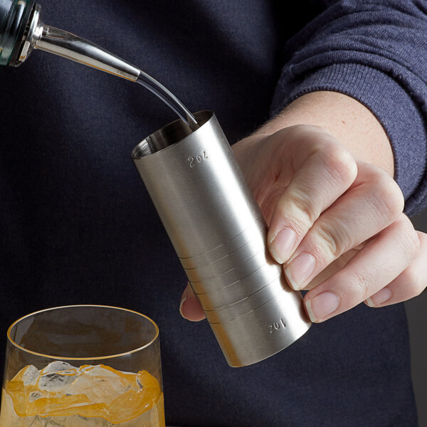 A man using a Franmara stainless steel thimble measure to pour liquid into a glass on a table in a cocktail bar.