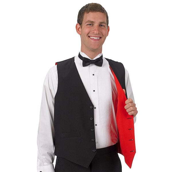 A man in a tuxedo holding a red and black reversible server vest.