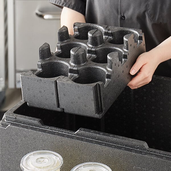 A person holding a black Cambro Cam GoBox cup holder with two cups inside.