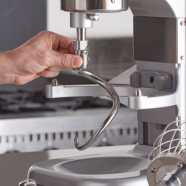 A hand using a metal dough hook attachment on an Avantco mixer.