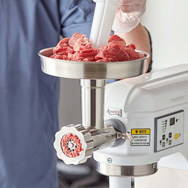 A gloved hand using an Avantco meat grinder attachment to grind meat.