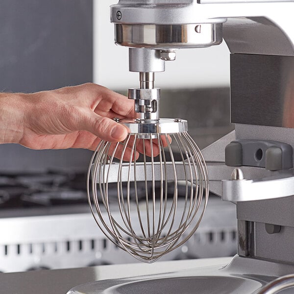 A person holding a wire whip attachment in front of a mixer.