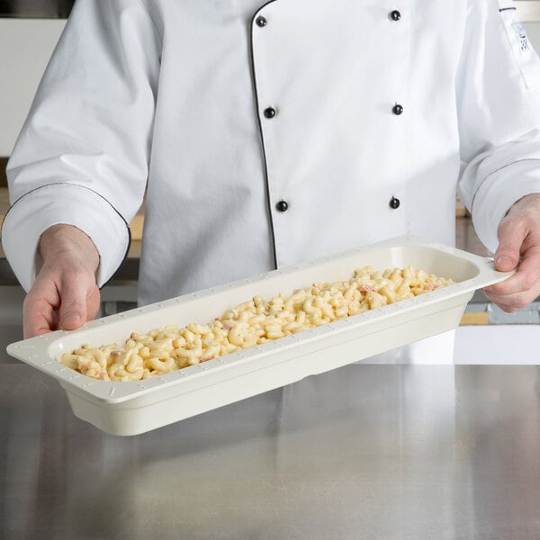 A chef holding a long ivory melamine food pan filled with macaroni and cheese.