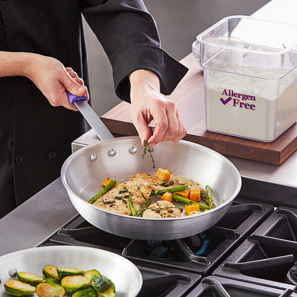 A person cooking brussels sprouts and meat in a Choice aluminum fry pan with a purple silicone handle.