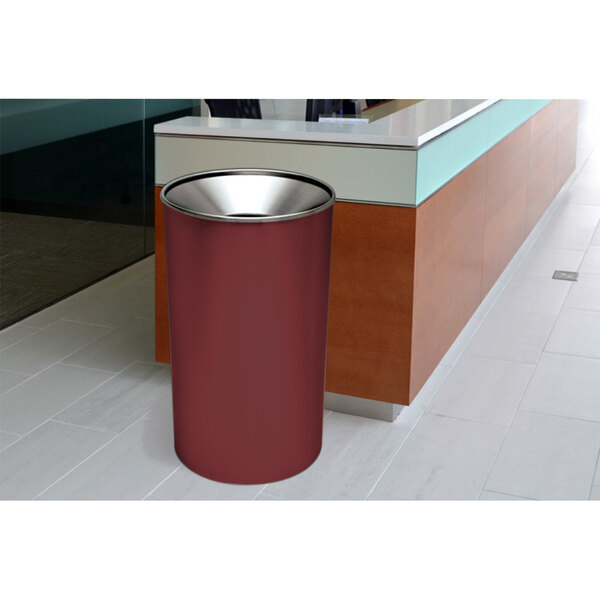 An Ex-Cell Kaiser burgundy steel round waste receptacle on a white counter with a silver edge.