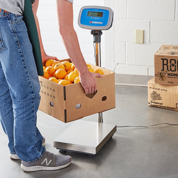 A person weighing a box of oranges on an AvaWeigh digital receiving scale.