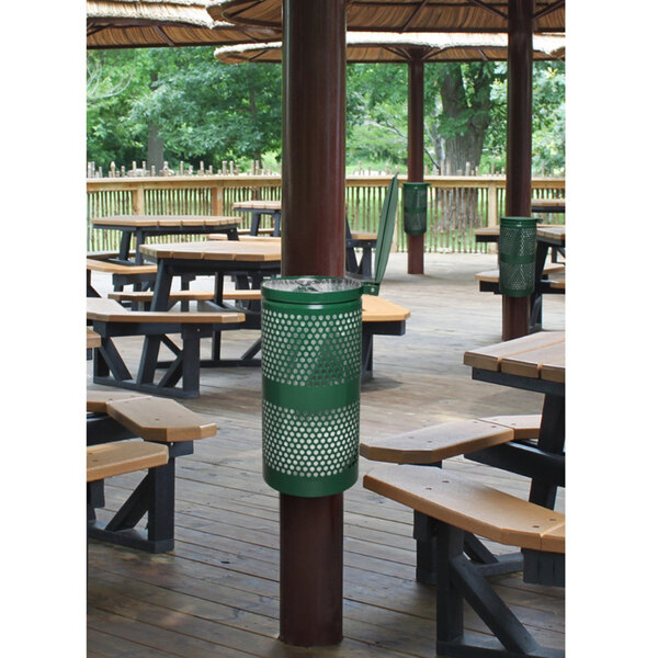 A picnic area with wooden tables and benches, and a green Ex-Cell Kaiser Landscape Series waste receptacle on a wood table.