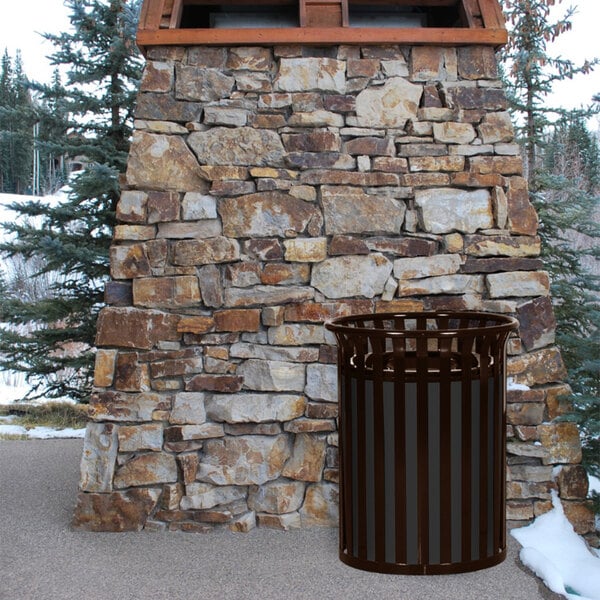A COF Streetscape Coffee gloss Ex-Cell Kaiser outdoor trash receptacle next to a stone wall.