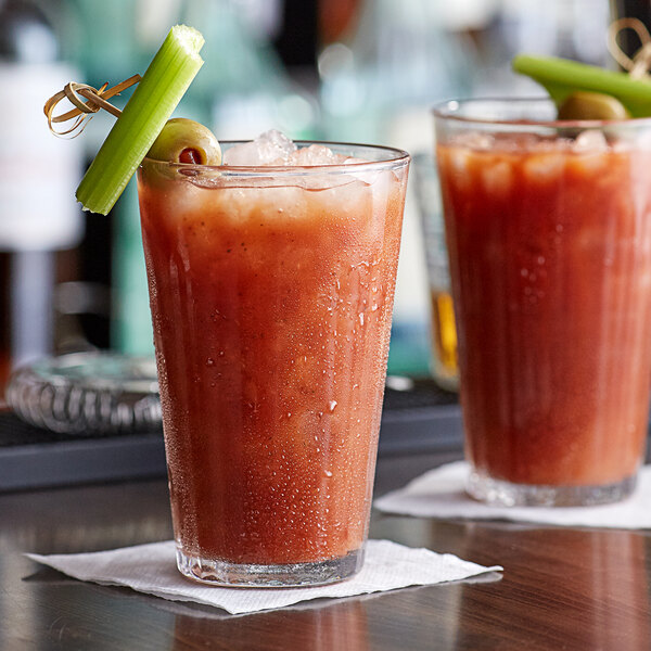 Two Duralex highball glasses filled with bloody marys garnished with celery and olives.