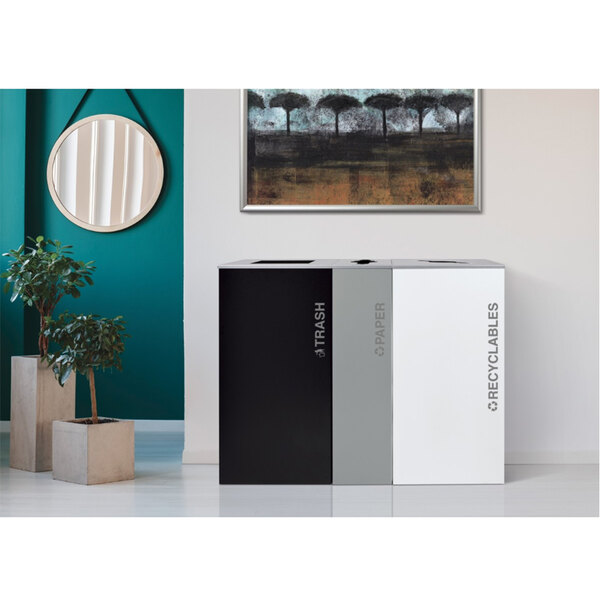 A black and white rectangular paper recycling receptacle next to a plant.