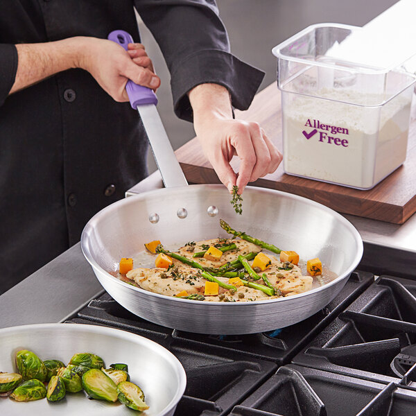 A person cooking food in a Choice aluminum fry pan with a purple handle.