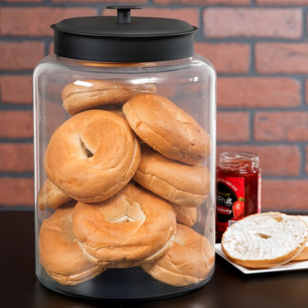 A glass Anchor Hocking Montana jar filled with bagels and jam on a counter.