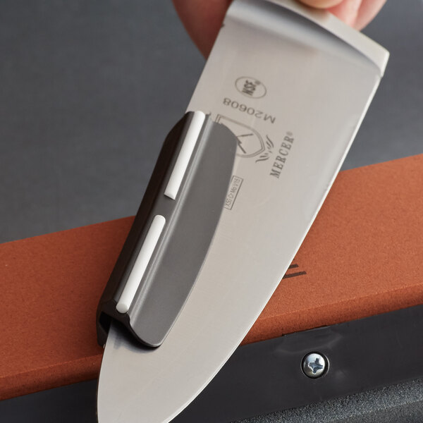 A person using a Mercer Culinary knife sharpening guide on a knife with a black handle.