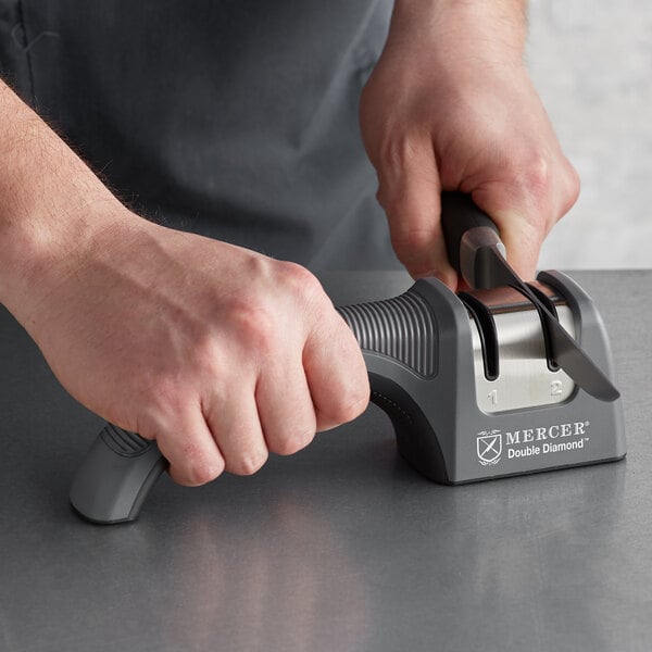A person using a Mercer Culinary knife sharpener to sharpen a knife on a counter.
