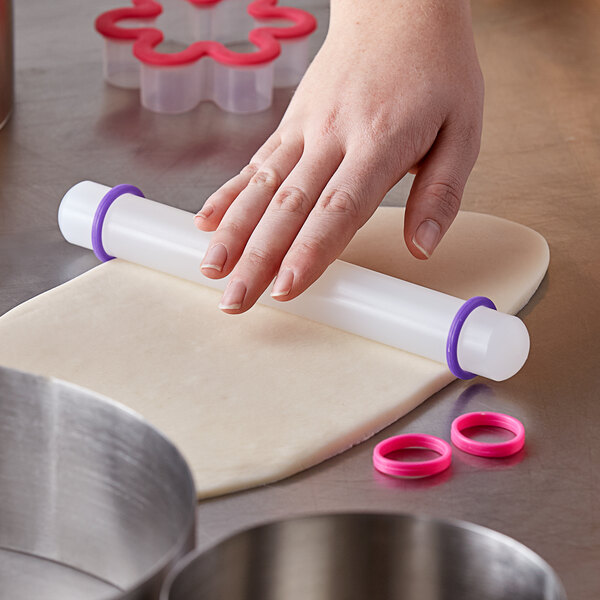 A person using an Ateco plastic French rolling pin with rings to roll out dough on a counter.