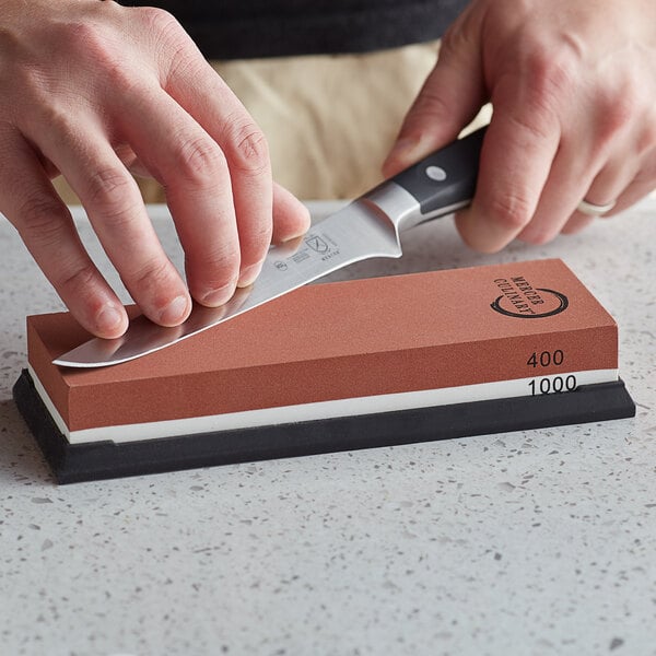 A person's hands using a Mercer Culinary combination sharpening stone to sharpen a knife.