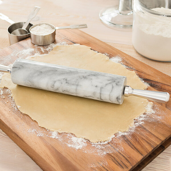 A white marble rolling pin with metal handles on a marble base.