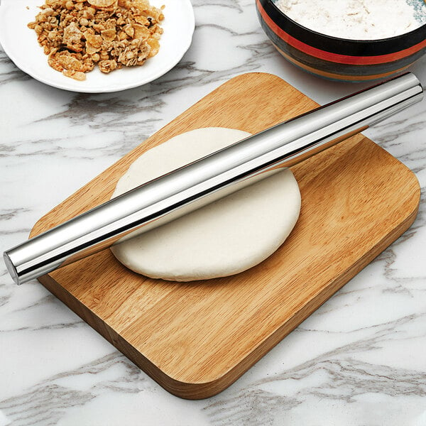 A Fox Run stainless steel tapered French rolling pin on pizza dough on a wooden board.