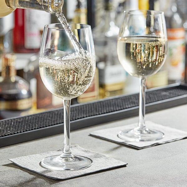 A person pouring wine into two Arcoroc wine glasses on a bar.