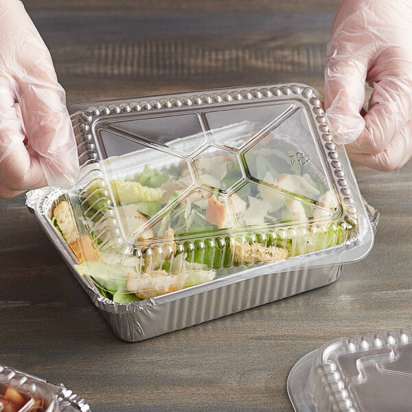A gloved hand holds a Choice clear dome lid on a plastic container of food.