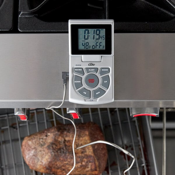 A piece of meat cooking on a grill with a CDN digital thermometer.