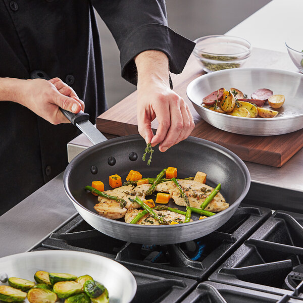 A person cooking asparagus and carrots in a Vollrath Arkadia non-stick fry pan.