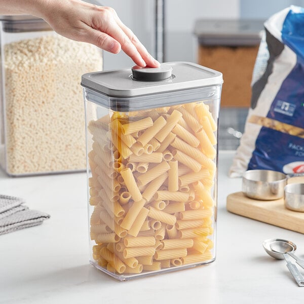 A person opening an OXO rectangular plastic food storage container with pasta inside.