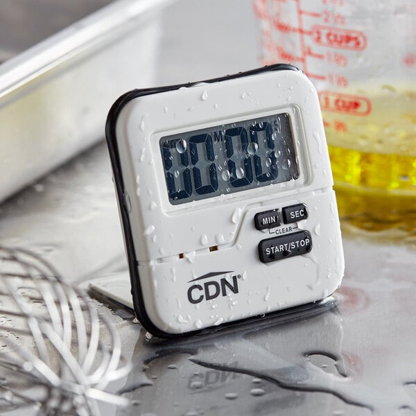 A white CDN digital kitchen timer on a counter with water drops.