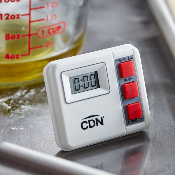 A white CDN digital kitchen timer with red buttons sitting on a counter.
