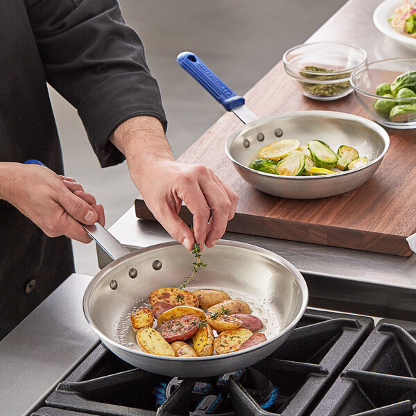 A person cooking brussels sprouts and herbs in a Vollrath Wear-Ever blue handled fry pan.