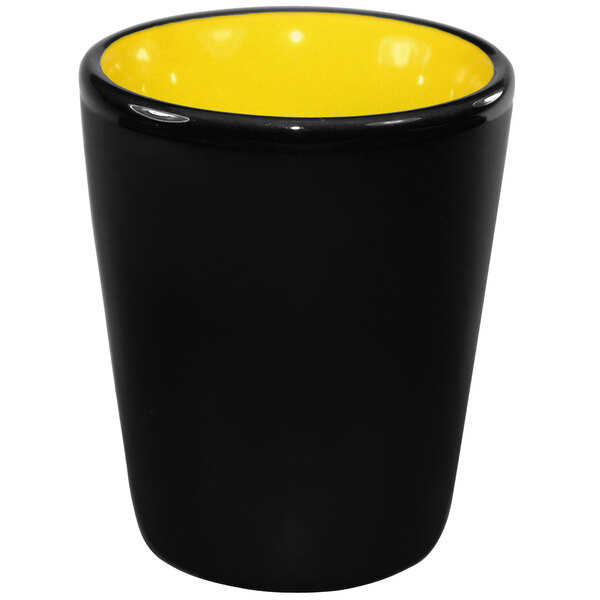 A yellow stoneware shot glass with a black interior and yellow rim.