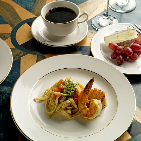 An International Tableware Florentine ivory stoneware plate with a gold rim, holding food and a cup of coffee.