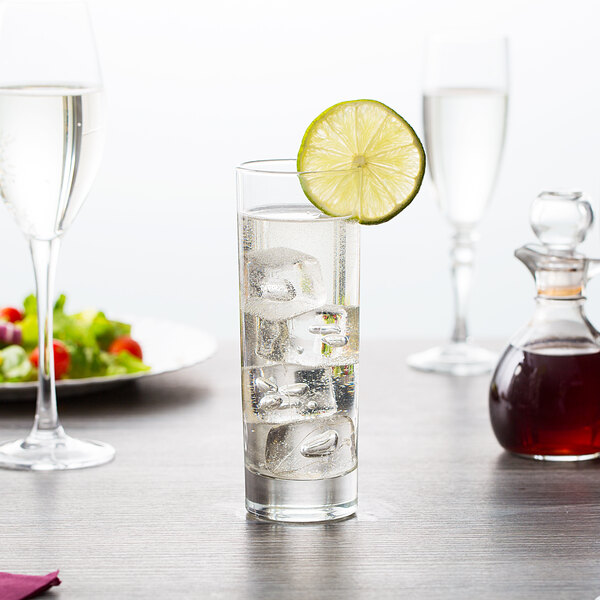 A close-up of an Arcoroc Islande highball glass filled with clear liquid and ice with a lime slice on the rim.
