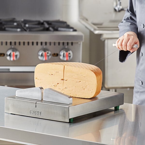 A person using a Garde stainless steel cheese blocker to cut a piece of cheese on a cutting board.