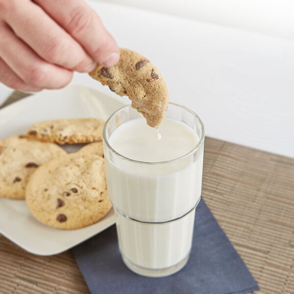 A hand holding a cookie over a stackable Arcoroc beverage glass of milk.