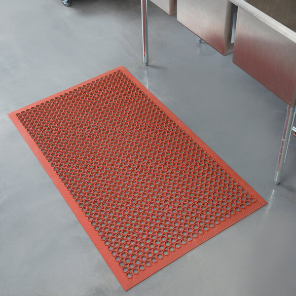 A red Notrax rubber floor mat with holes in it.