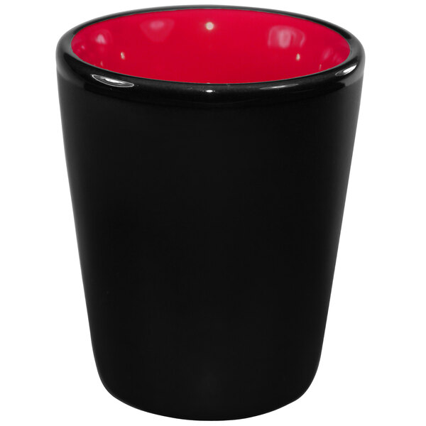 A black stoneware shot glass with a red interior and red rim.
