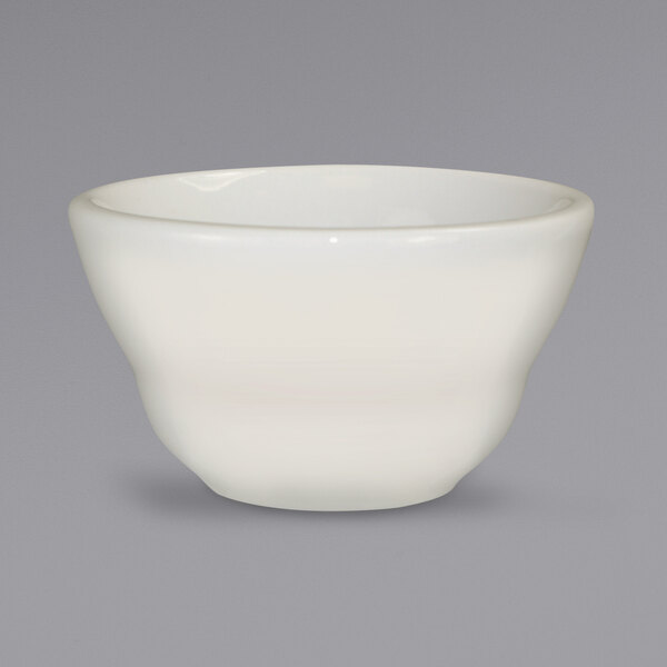 A close up of an International Tableware Roma ivory stoneware bowl on a gray background.