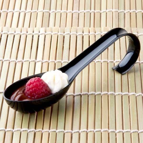 A Fineline Tiny Tensils black plastic spoon with a raspberry and whipped cream on it.