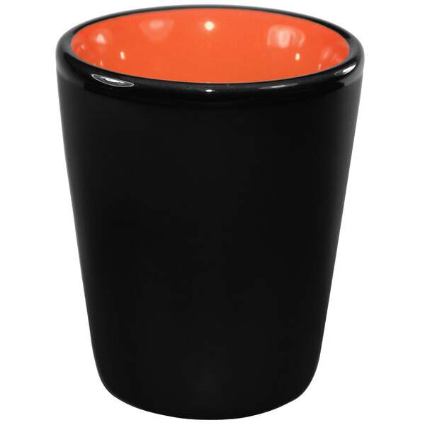 An orange stoneware shot glass with a black rim.