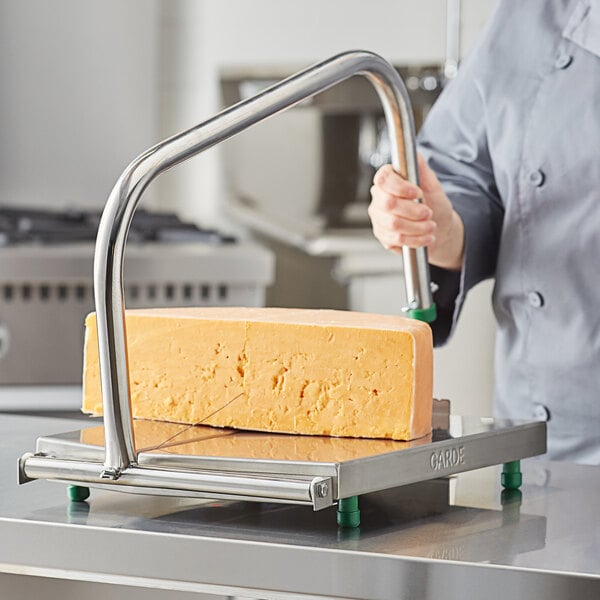 A person in a chef's uniform using a Garde Large Cheese Blocker to cut a large block of cheese.